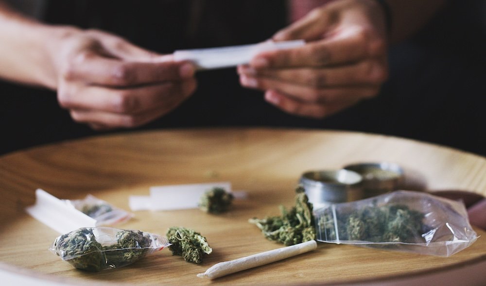 Person rolling a joint over a table with indica flower.